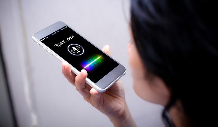 A person holds a smart phone up to their mouth to conduct a voice search.